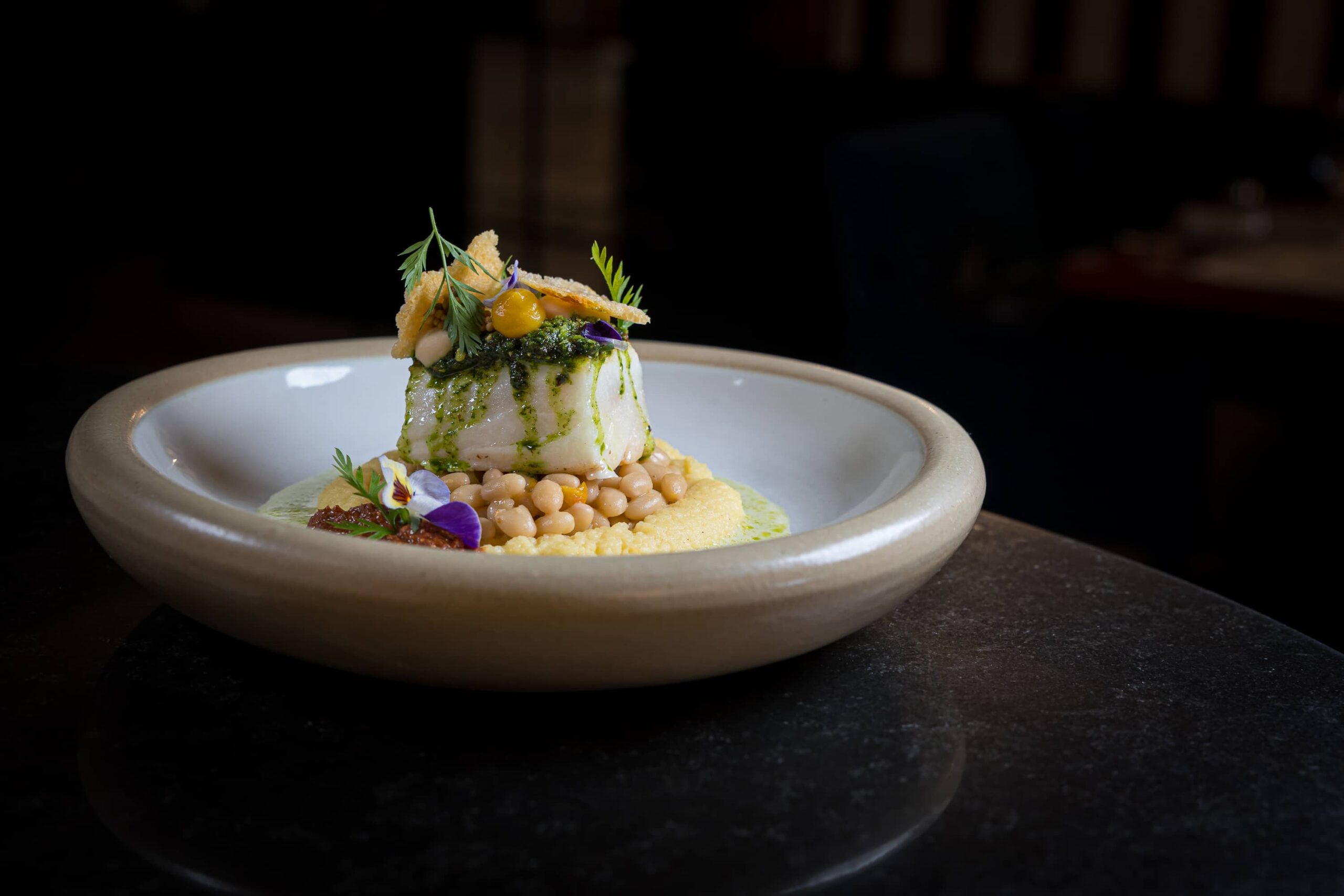 Ein kunstvoll angerichteter Teller mit einem Gericht aus Püree, Kichererbsen und frischen Kräutern.