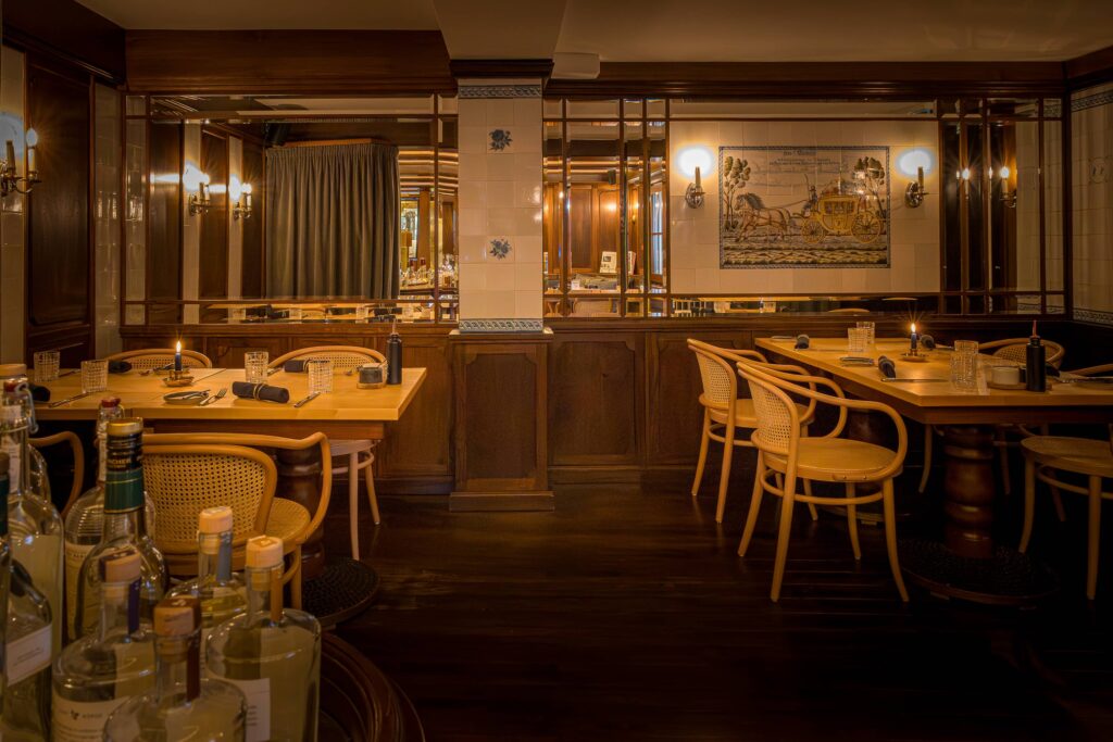 Innenansicht eines Restaurants mit Holztischen und Stühlen sowie einer Bar im Vordergrund.