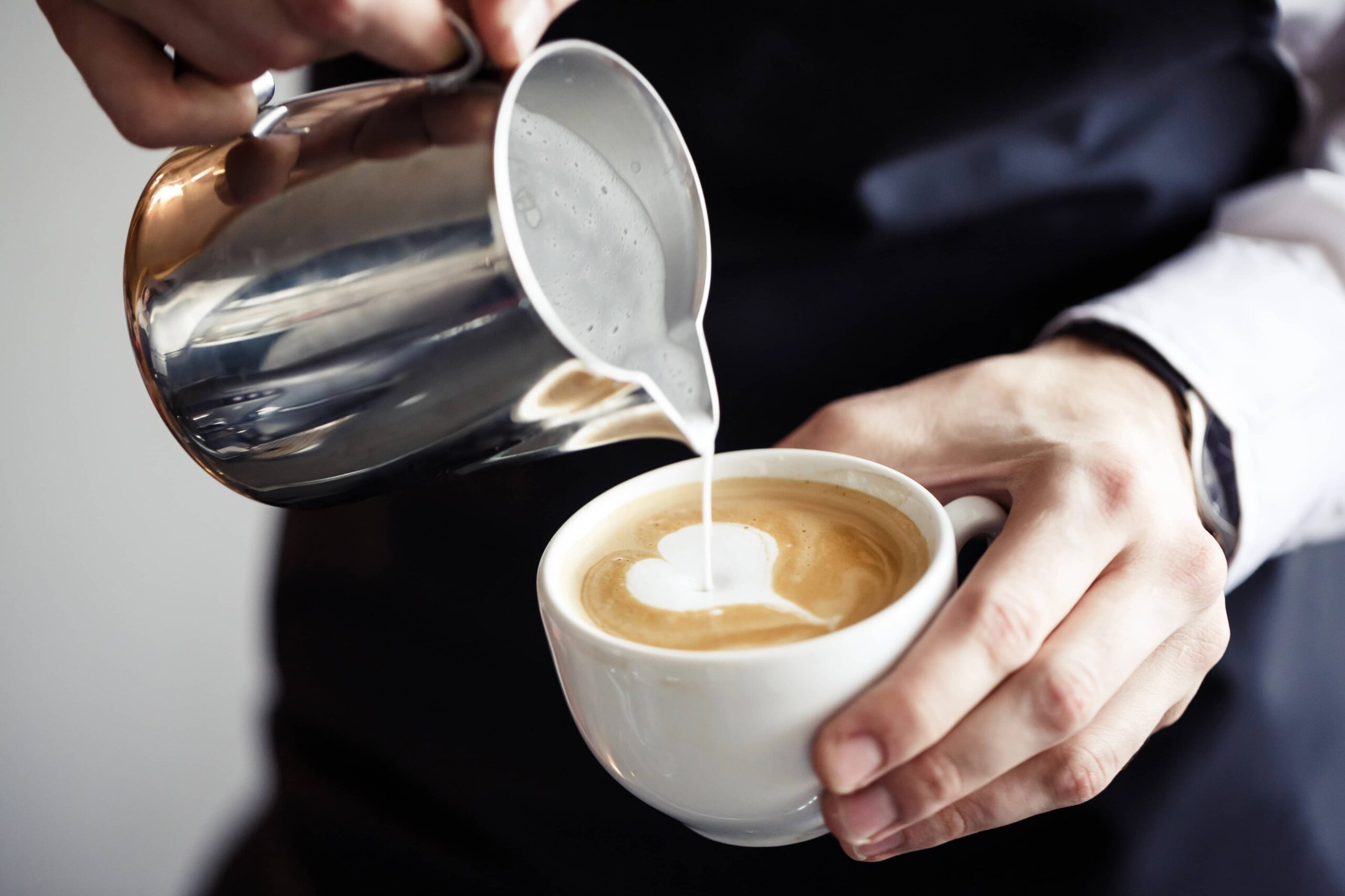 Ein Barista gießt Milch in einen Becher mit Kaffee, um ein Herzmuster zu erstellen.