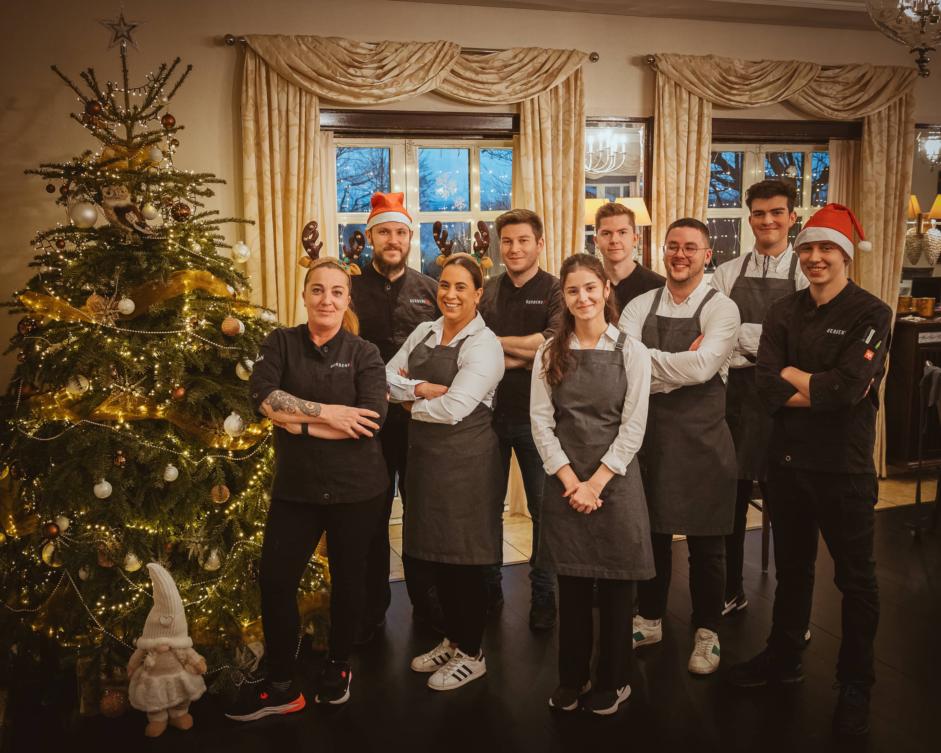 Gruppe von Köchen in Arbeitskleidung vor einem festlich geschmückten Weihnachtsbaum.