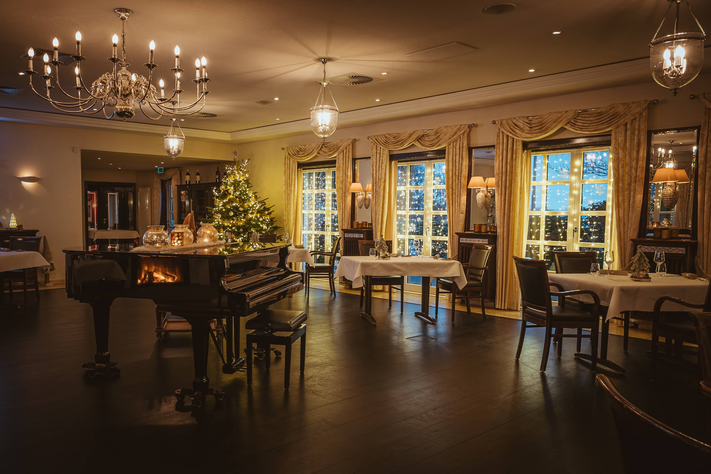 Elegantes Restaurant mit Klavier, festlich dekoriert und beleuchtet, mit Fenstern, die einen Blick auf die Weihnachtsbeleuchtung bieten.