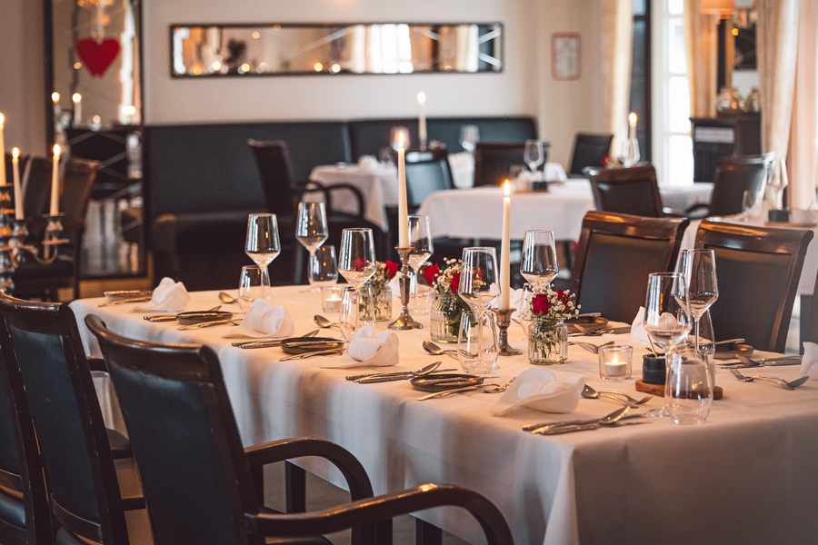 Elegante gedeckte Tafel mit Kerzen, Gläsern und Blumenarrangements in einem Restaurant.